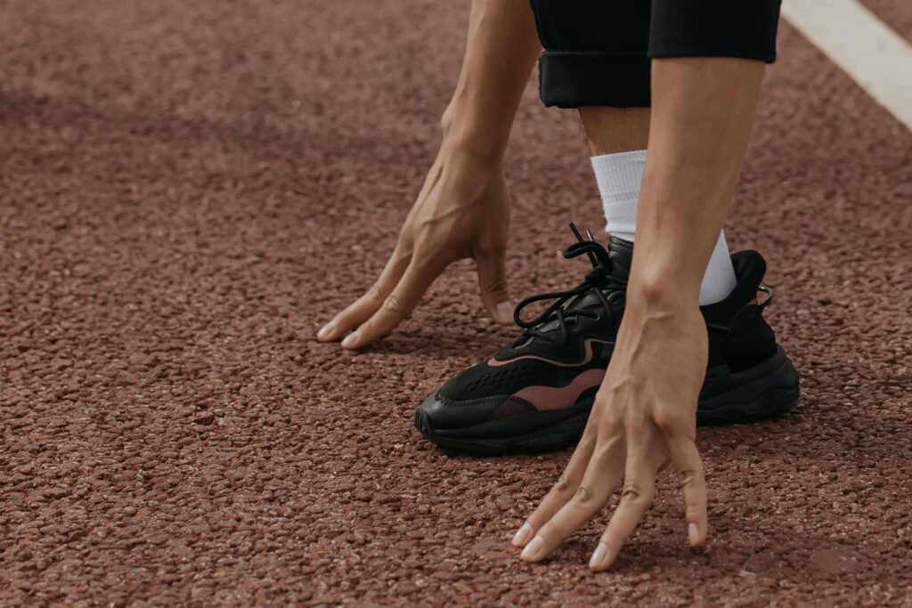 A runner wearing black sneakers is positioned on a track, poised for action, highlighting athletic readiness.