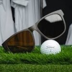 Sunglasses and a golf ball resting on green grass inside a room, creating a playful indoor golf scene.